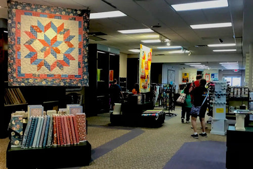 Colorful star-pattern quilt with orange, blue and peach tones hangs on display.