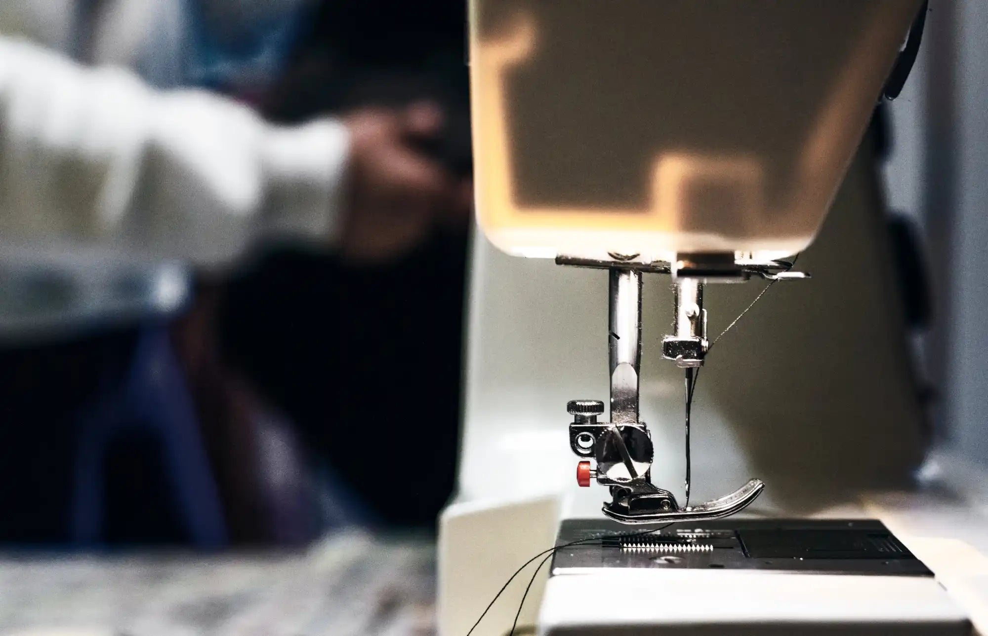 Sewing machine needle and presser foot in close-up detail.