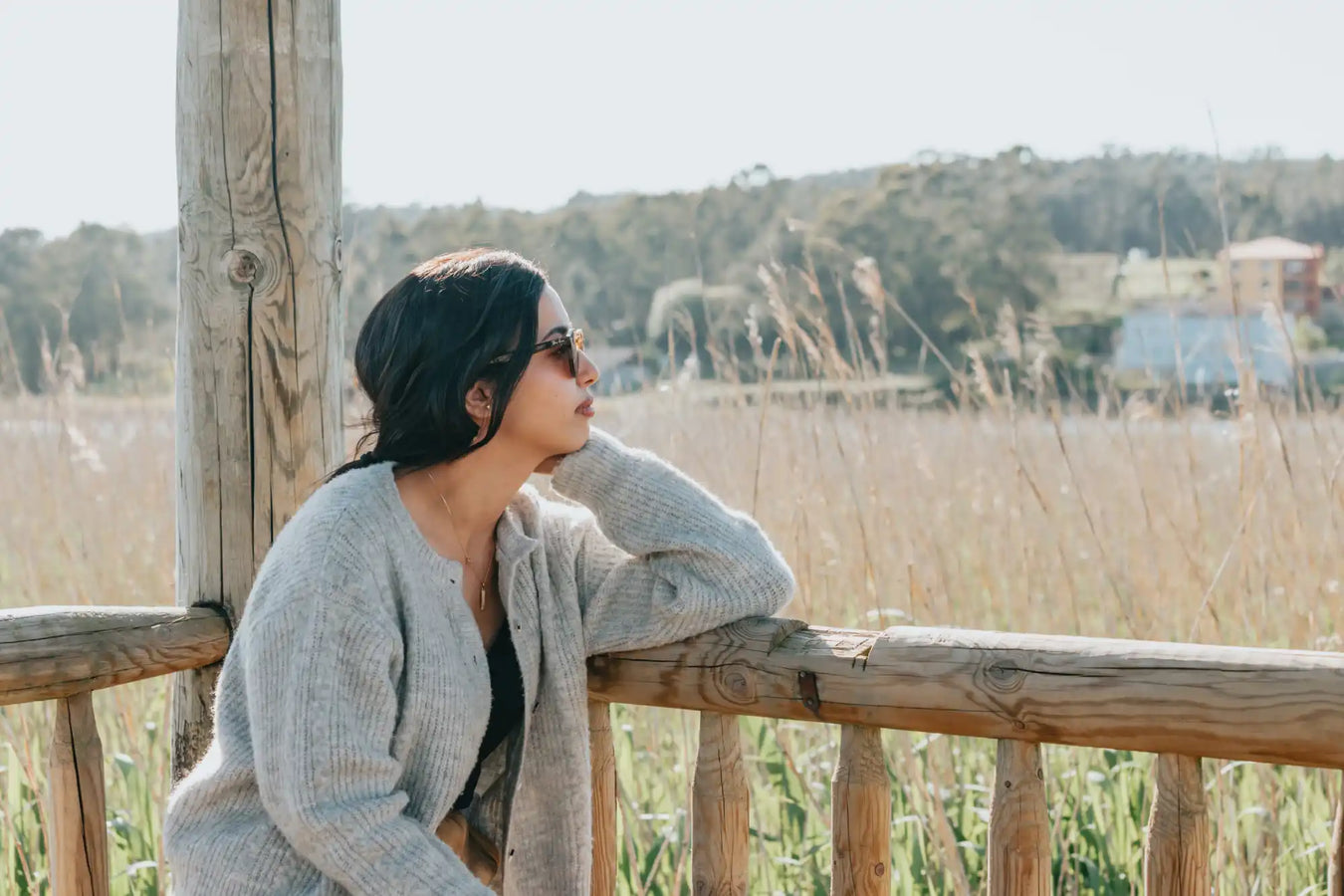 Person wearing a cozy gray cardigan and beanie while leaning on a wooden railing.